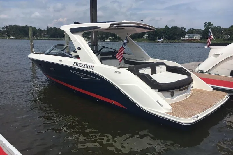 The Image of 2017 Sea Ray SLX 310 boat docked on a calm lake with American flags. - 1