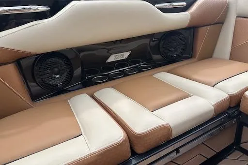 Slide: The Image of 2024 Supreme S220 boat interior with tan and cream seating, featuring built-in speakers. - 14