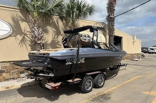 Slide: The Image of 2024 Supreme S220 boat on trailer, parked near palm trees and building. - 3