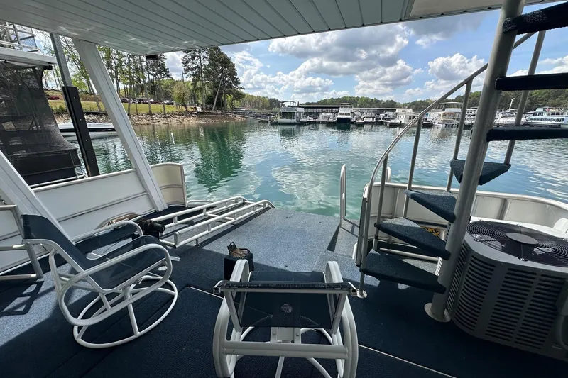 Slide: The Image of 1998 Stardust Cruisers 16x84 houseboat deck with chairs, spiral staircase, and scenic lake view. - 13