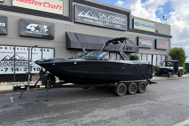 The Image of 2024 MasterCraft X24 boat on trailer outside California Custom dealership. - 0
