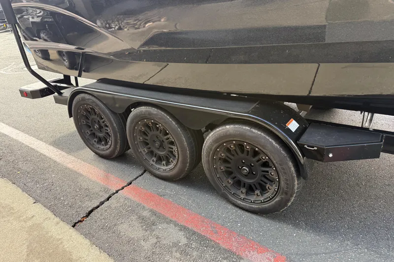 Slide: The Image of 2024 MasterCraft X24 boat trailer with triple black wheels on pavement. - 11