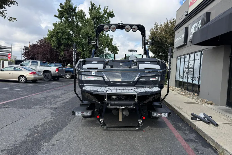 Slide: The Image of 2024 MasterCraft X24 boat parked in a lot, rear view with trees and buildings. - 3