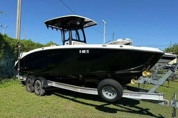 Slide: The Image of 2021 Yamaha Boats 255 FSH Sport E on trailer, black hull, sunny day. - 3