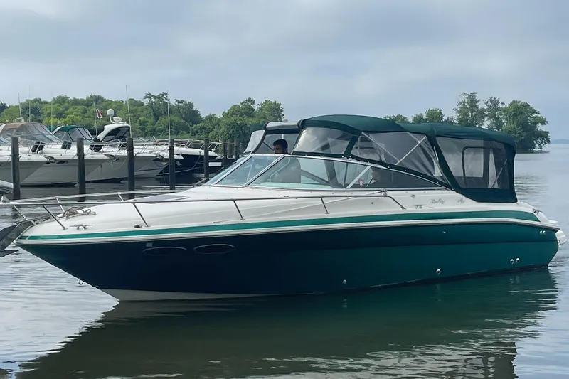 The Image of 2001 Sea Ray 280 Sun Sport boat docked on calm water, surrounded by lush greenery. - 0