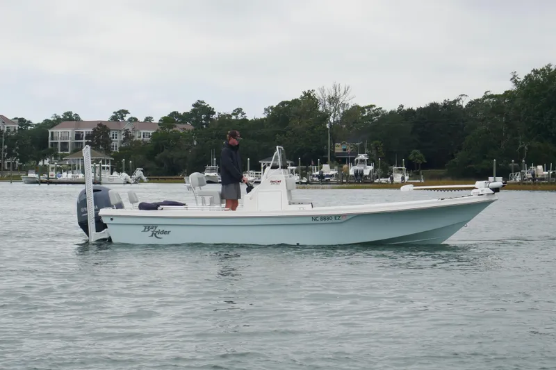 Slide: The Image of 2023 Bay Rider 239 Bay boat on water with person standing, surrounded by trees and buildings. - 4