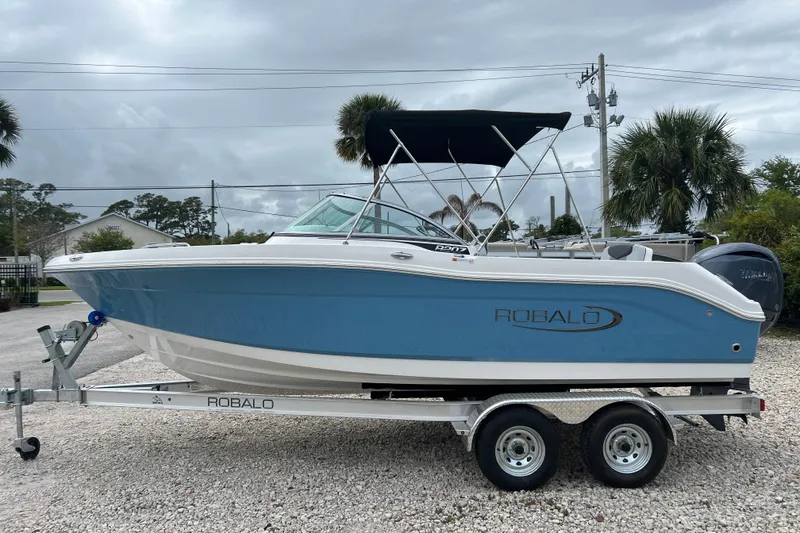 The Image of 2026 Robalo R207 Dual Console boat on trailer, blue and white design, parked outdoors. - 1