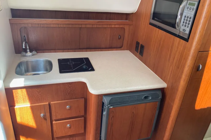 Slide: The Image of Compact galley in 2002 Tiara Yachts 2900 Open, featuring sink, stove, microwave, and wood cabinetry. - 59
