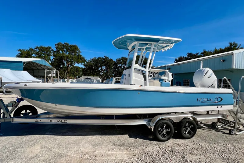 Slide: The Image of 2026 Robalo 246 Cayman boat on trailer, blue hull, parked outdoors under clear sky. - 5