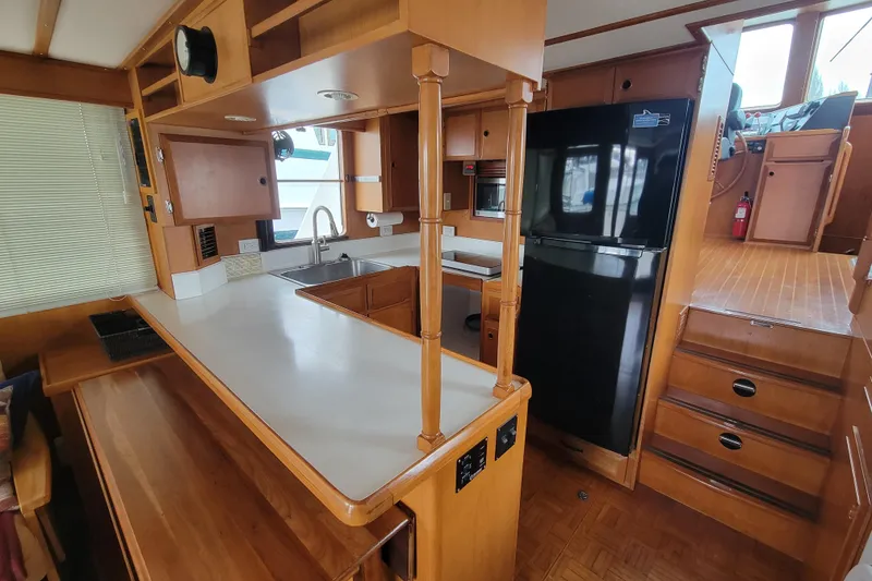 Slide: The Image of 2001 DeFever Pilothouse kitchen with wooden cabinetry, black refrigerator, and stairs leading up. - 22