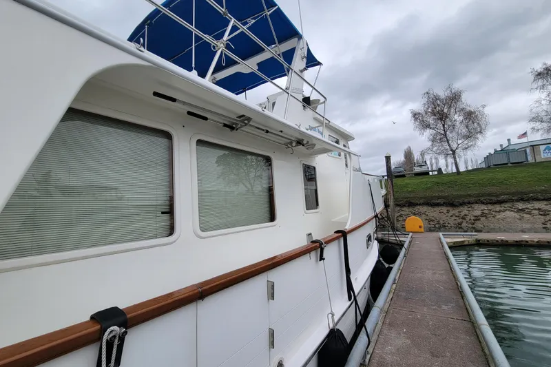 Slide: The Image of 2001 DeFever Pilothouse yacht docked at marina, featuring blue canopy and wooden railings. - 4