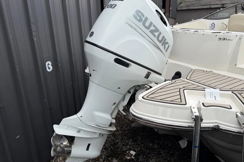 Slide: The Image of 2022 Stingray 231 DC boat with Suzuki outboard motor, docked near a metal wall. - 7