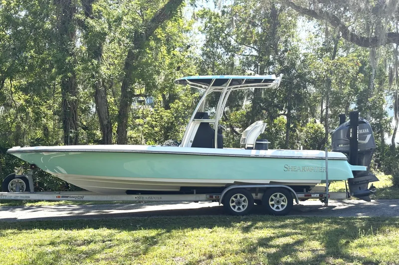 The Image of 2018 ShearWater 26 Carolina boat on trailer, surrounded by lush trees. - 0