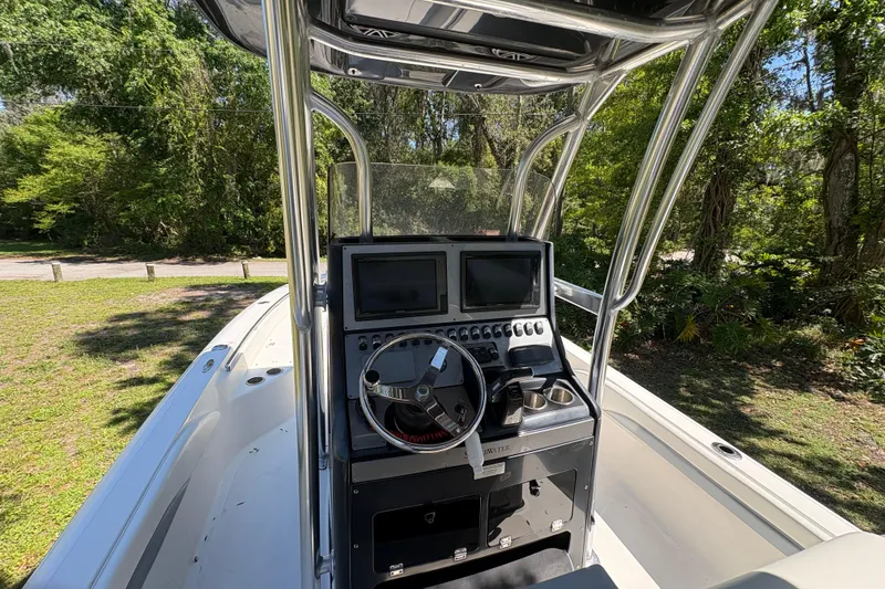 Slide: The Image of 2018 ShearWater 26 Carolina boat console with dual screens and steering wheel, surrounded by greenery. - 12