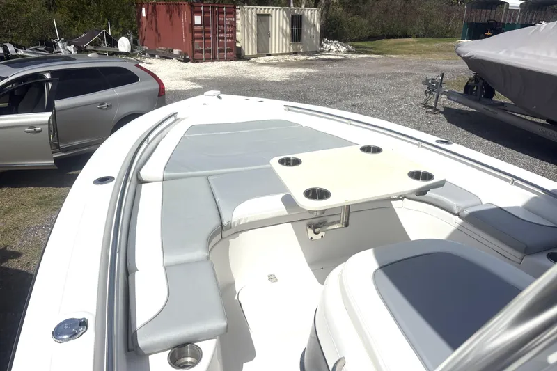 Slide: The Image of 2018 ShearWater 26 Carolina boat interior with seating and table, parked near a silver car. - 5