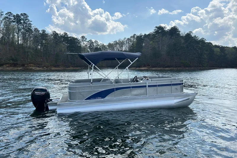 Slide: The Image of 2023 Bennington 22 SSR pontoon boat on a serene lake with a Mercury outboard motor. - 5