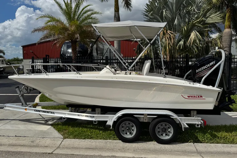Slide: The Image of 2017 Boston Whaler 170 Super Sport boat on trailer, parked outdoors with palm trees. - 21