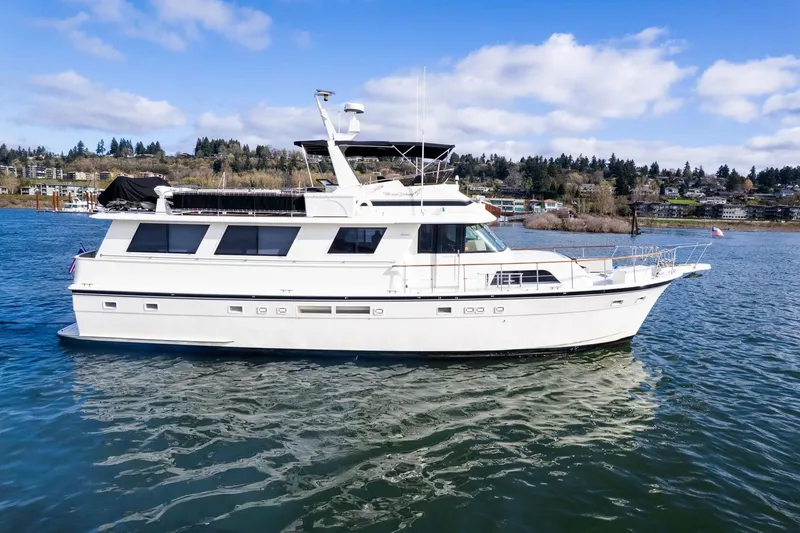 The Image of 1986 Hatteras 63 Motor Yacht cruising on a scenic lake under a clear blue sky. - 0