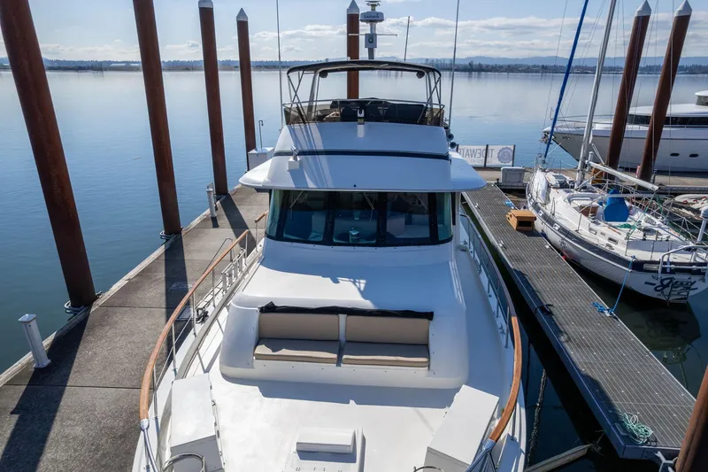 Slide: The Image of 1986 Hatteras 63 Motor Yacht docked at marina, surrounded by calm water and sailboats. - 150