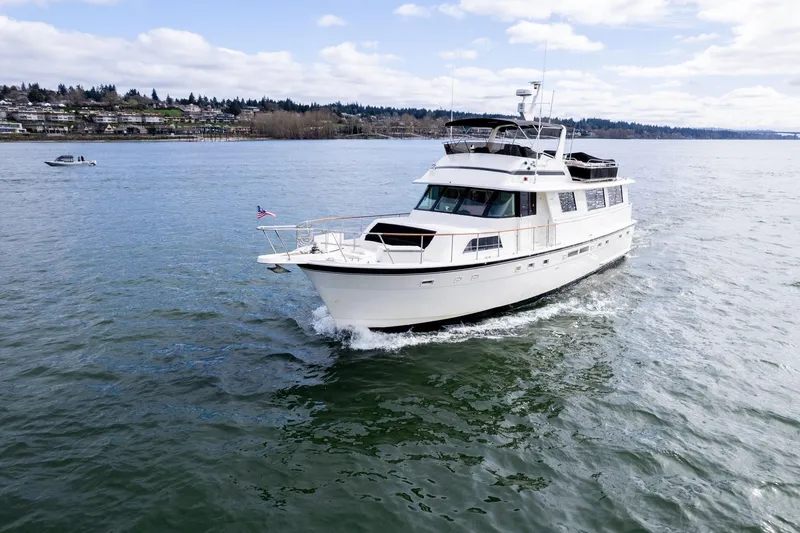 Slide: The Image of 1986 Hatteras 63 Motor Yacht cruising on a scenic lake under a partly cloudy sky. - 160