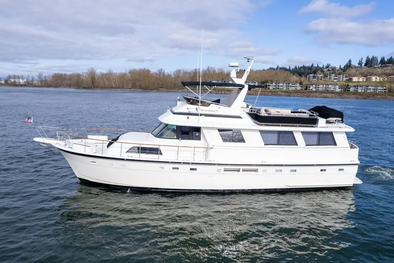Slide: The Image of 1986 Hatteras 63 Motor Yacht cruising on a calm river under a cloudy sky. - 163