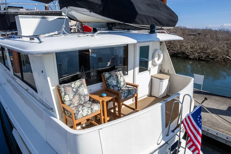 Slide: The Image of 1986 Hatteras 63 Motor Yacht with deck seating and American flag, docked by water. - 96