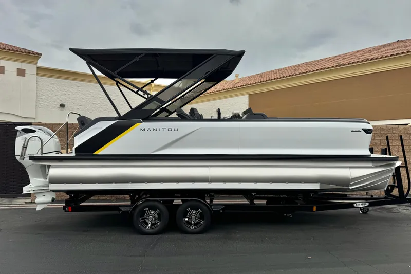 The Image of 2025 Manitou EXPLORE 24 pontoon boat on trailer, featuring sleek design and canopy. - 0