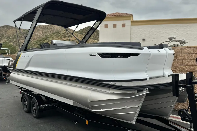 Slide: The Image of 2025 Manitou EXPLORE 24 pontoon boat on trailer, sleek design, outdoor setting. - 1