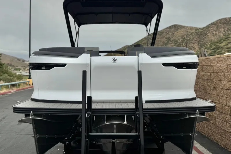 Slide: The Image of 2025 Manitou EXPLORE 24 pontoon boat, rear view, parked near mountains. - 2