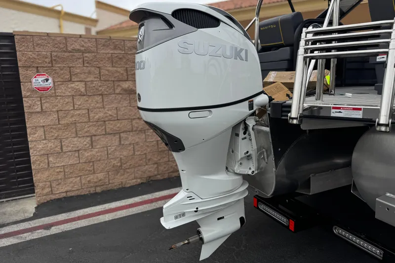 Slide: The Image of 2025 Manitou EXPLORE 24 with Suzuki outboard motor, parked near a brick wall. - 7