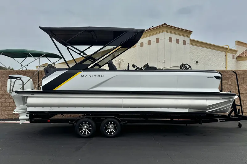 The Image of 2025 Manitou EXPLORE 24 pontoon boat on trailer, sleek design, black canopy. - 0