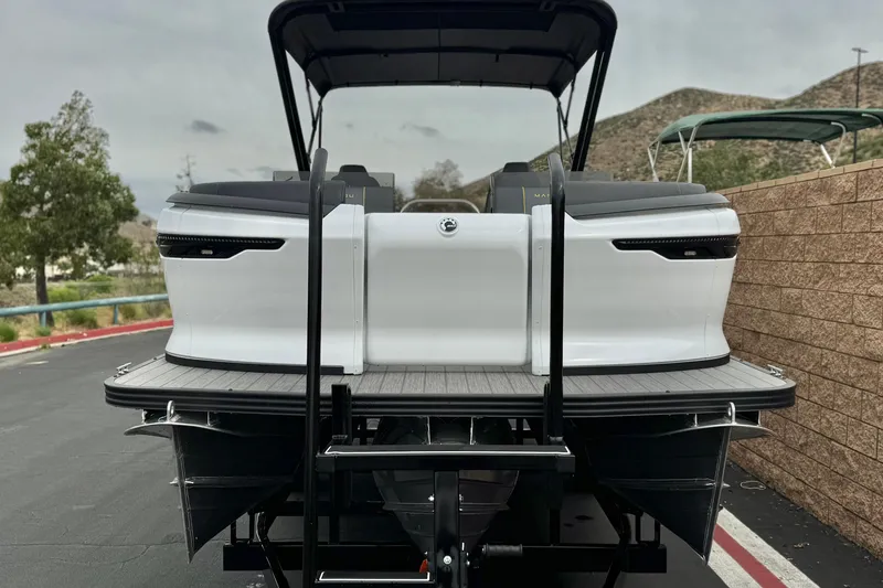 Slide: The Image of 2025 Manitou EXPLORE 24 pontoon boat, rear view, parked outdoors. - 2