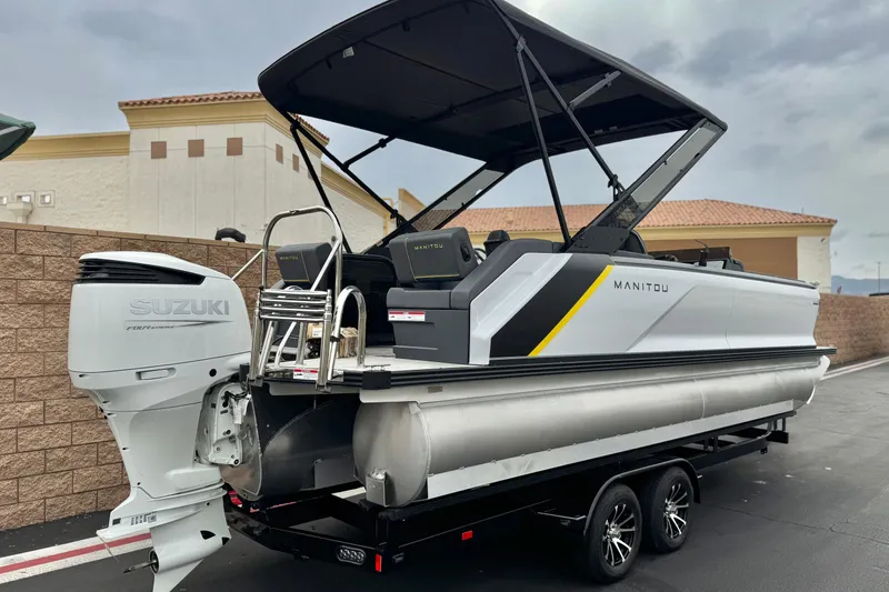 Slide: The Image of 2025 Manitou EXPLORE 24 pontoon boat with Suzuki outboard motor, parked on trailer. - 6
