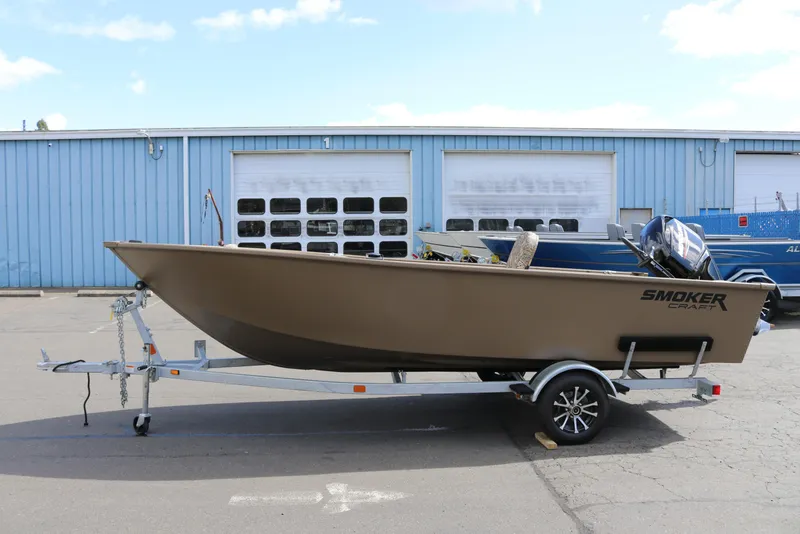 Slide: The Image of 2026 Smoker Craft Freedom 160 TL boat on trailer, parked outside a blue warehouse. - 4