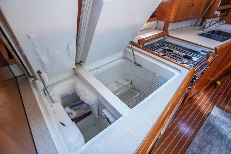 Slide: The Image of Jeanneau Sun Odyssey 45.2 yacht kitchen with open freezer, stove, and wooden cabinetry. - 49