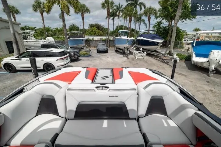 Slide: The Image of 2019 MasterCraft XStar boat interior with red and gray seating, parked near palm trees and vehicles. - 11
