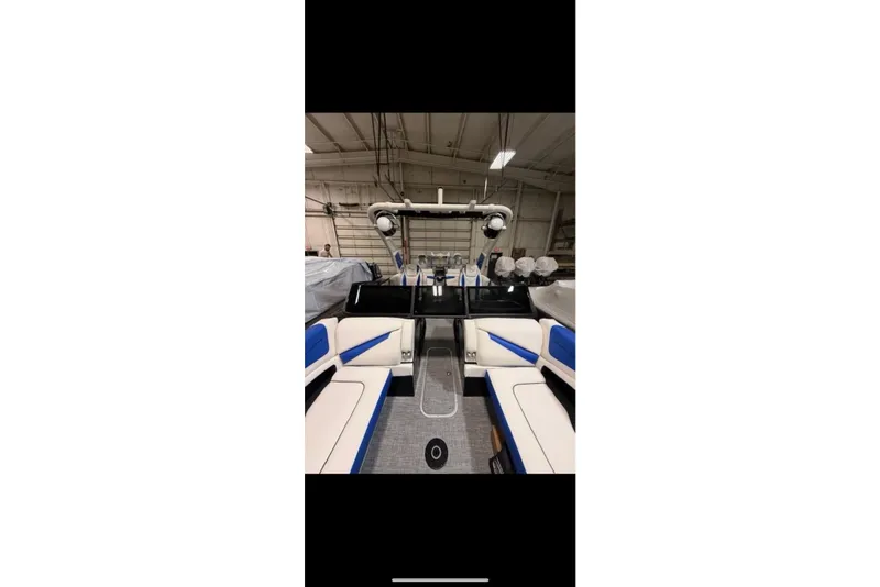 Slide: The Image of 2026 South Bay 25 Sport Twin boat interior with blue and white seating in a warehouse. - 18