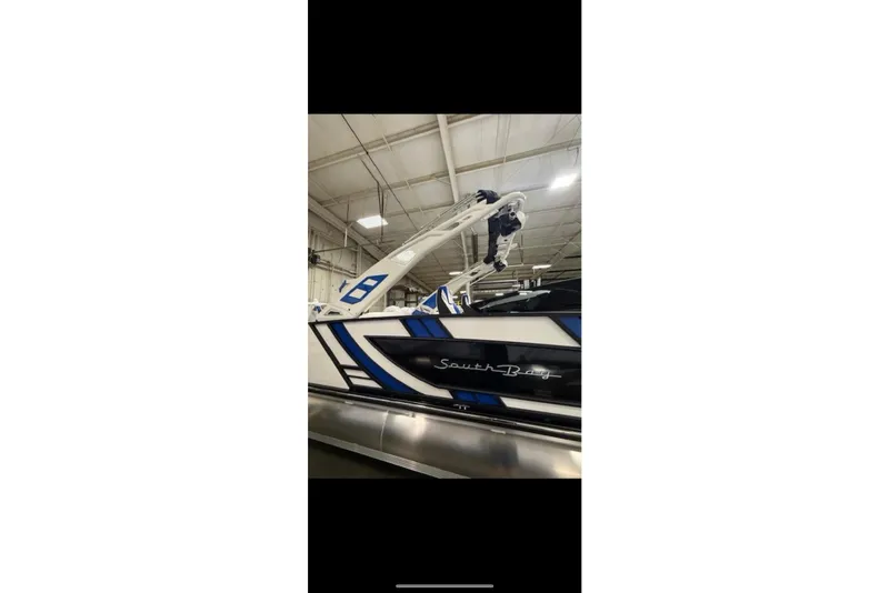 Slide: The Image of 2026 South Bay 25 Sport Twin boat in a showroom, featuring sleek blue and white design. - 29