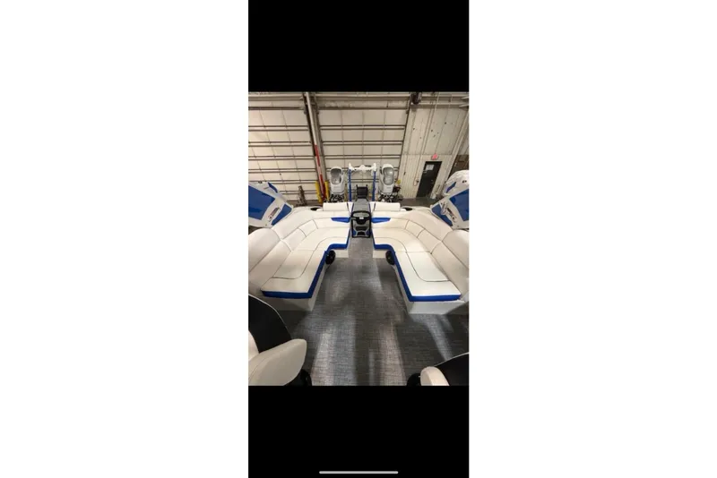 Slide: The Image of 2026 South Bay 25 Sport Twin boat interior with white and blue seating in a garage. - 38