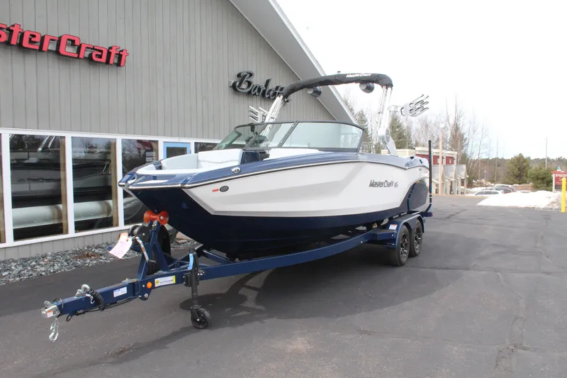 Slide: The Image of 2026 MasterCraft NXT23 boat on trailer in front of building. - 3