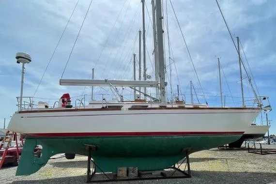 The Image of 1983 Bristol 38.8 sailboat on dry dock, white hull with red stripe, clear sky background. - 0