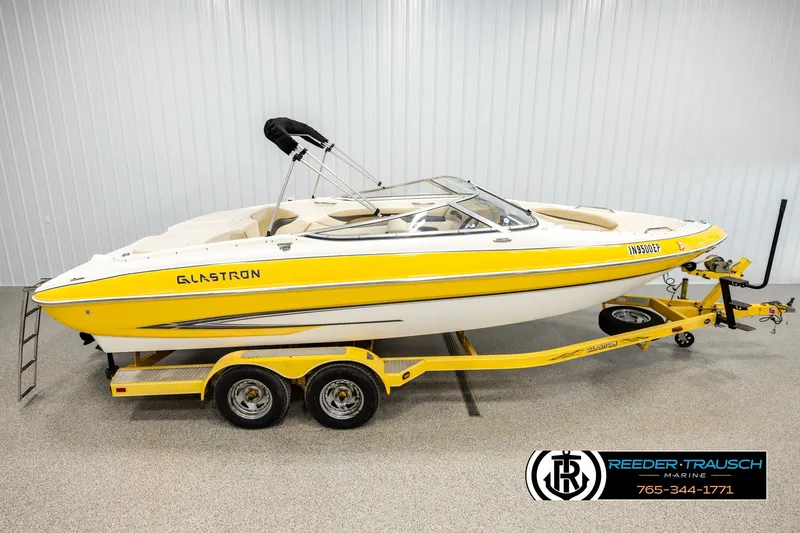 The Image of 2006 Glastron GX 235 boat in yellow on a matching trailer, indoor display. - 1