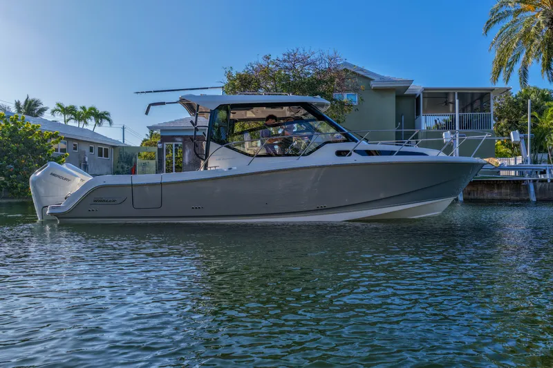 The Image of 2025 Boston Whaler 325 Conquest boat on calm water near waterfront homes. - 1