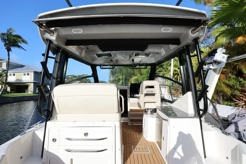 Slide: The Image of 2025 Boston Whaler 325 Conquest boat interior with seating and helm, docked by a canal. - 16