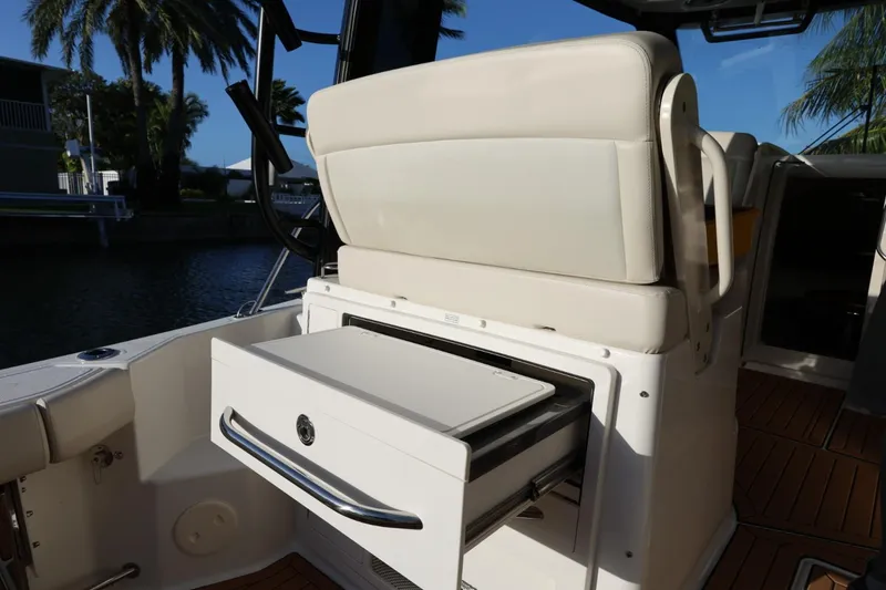 Slide: The Image of 2025 Boston Whaler 325 Conquest boat interior with open storage drawer, palm trees in background. - 17