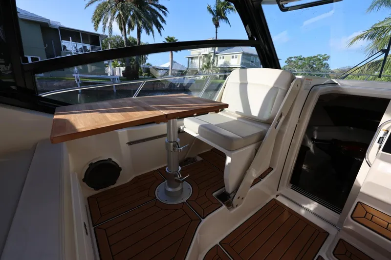 Slide: The Image of 2025 Boston Whaler 325 Conquest interior with wooden table and seating, docked near palm trees. - 22