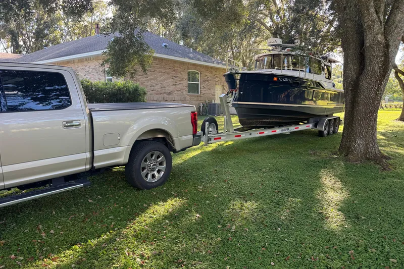 Slide: The Image of Truck towing 2024 Ranger Tugs R-27 boat on a trailer in a grassy yard. - 100