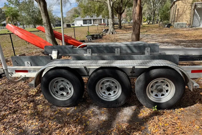 Slide: The Image of Triple-axle trailer for 2024 Ranger Tugs R-27, parked outdoors with trees and leaves. - 102