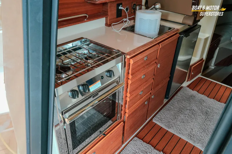 Slide: The Image of 2024 Ranger Tugs R-27 interior kitchen with stove, wooden cabinetry, and compact design. - 42