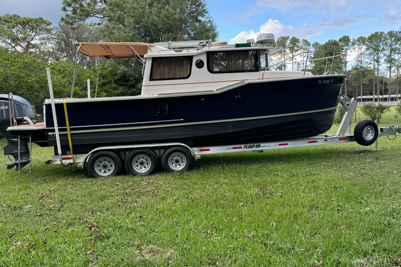 Slide: The Image of 2024 Ranger Tugs R-27 boat on trailer, parked on grass with trees in background. - 97